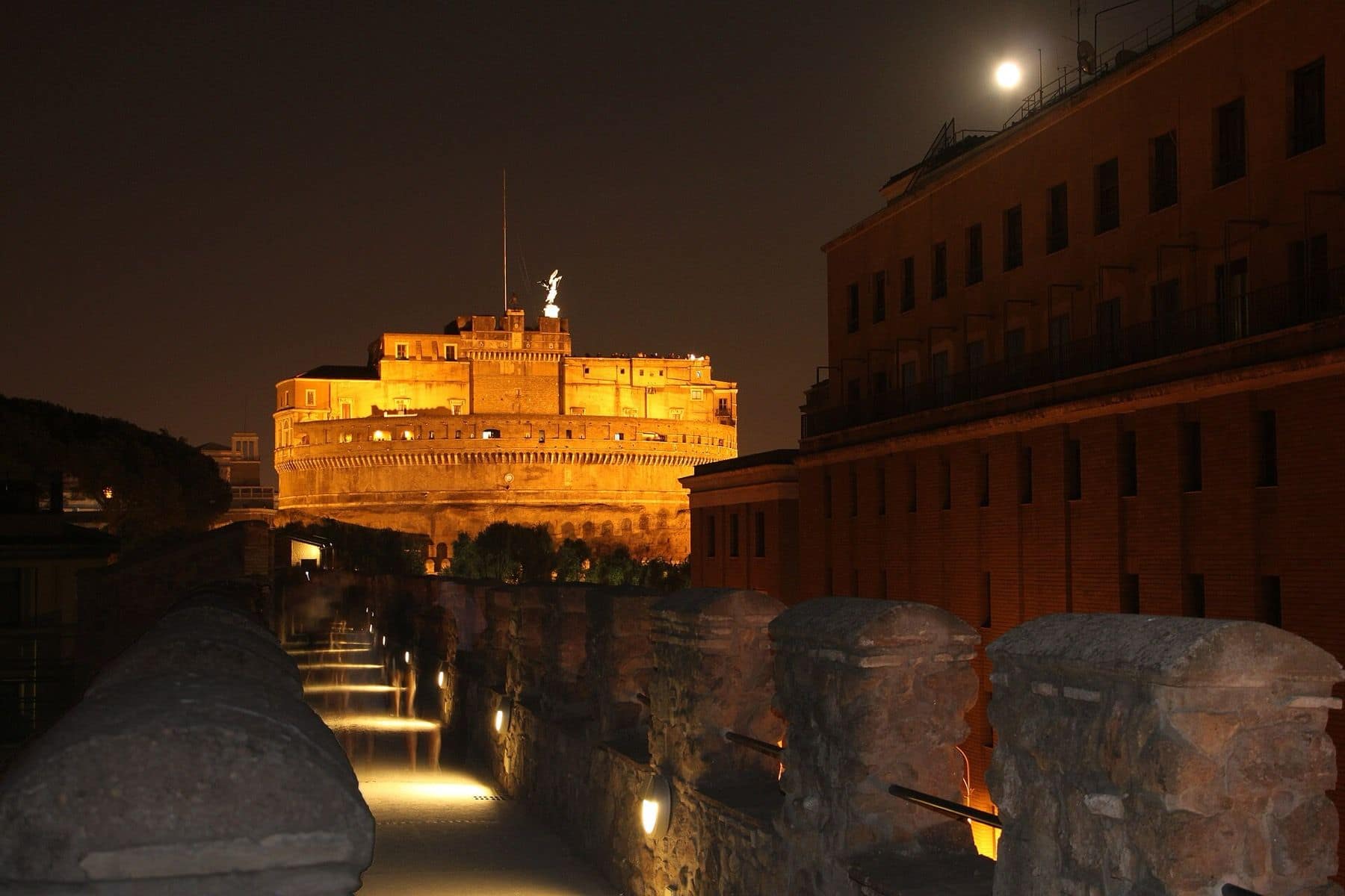 Le Passetto di Borgo illuminé de nuit, avec le château Saint-Ange éclairé en arrière-plan.