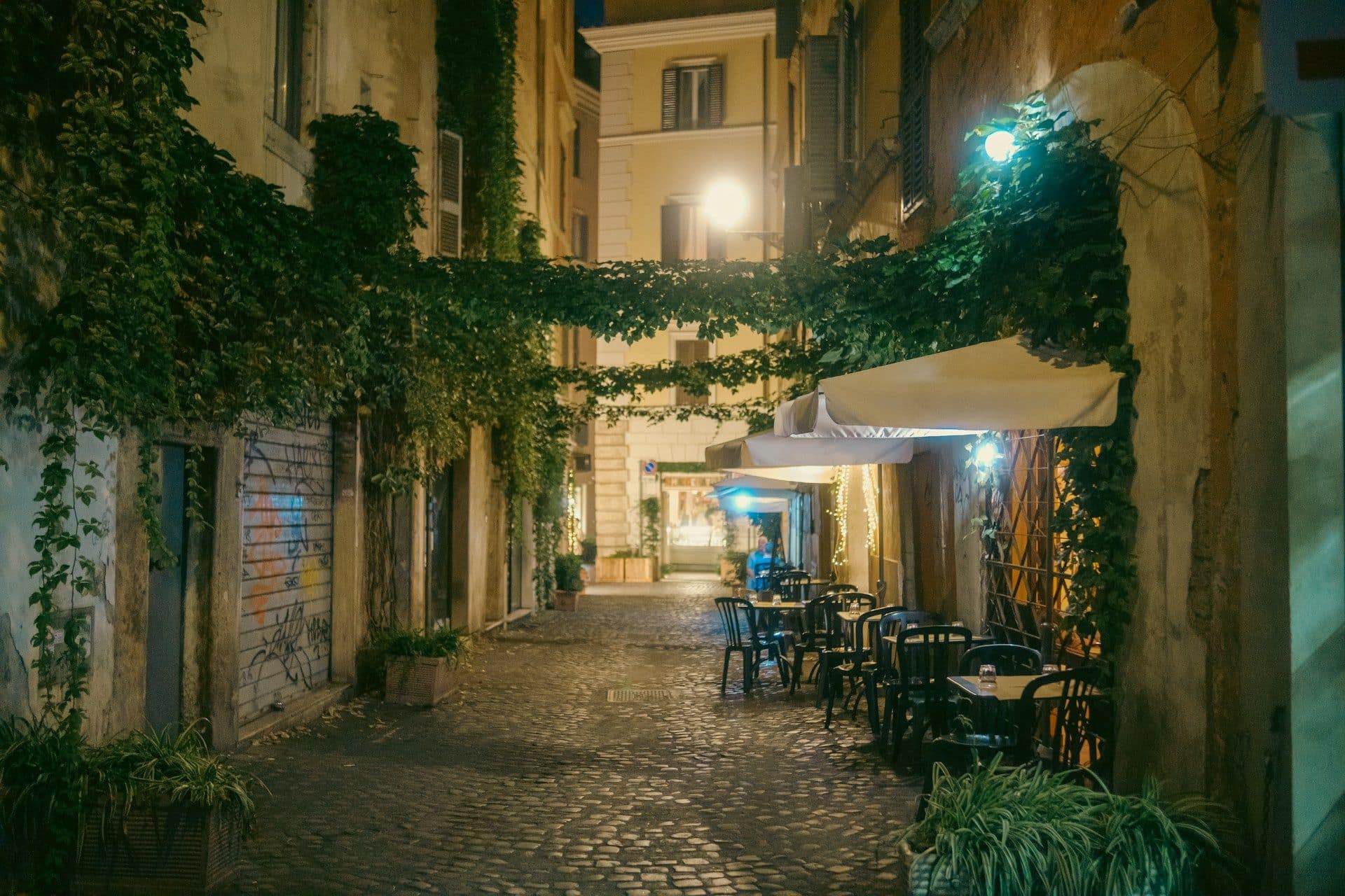 Une ruelle pavée du Trastevere la nuit, façades ocre et lanternes allumées.